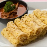 Roti Jala yang digulung rapi, siap disajikan bersama kuah kari yang menggugah selera, mencerminkan warisan kuliner Melayu yang kaya dan penuh cita rasa