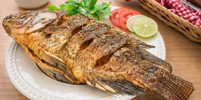 Ikan nila goreng berwarna keemasan disajikan dengan sambal dan lalapan